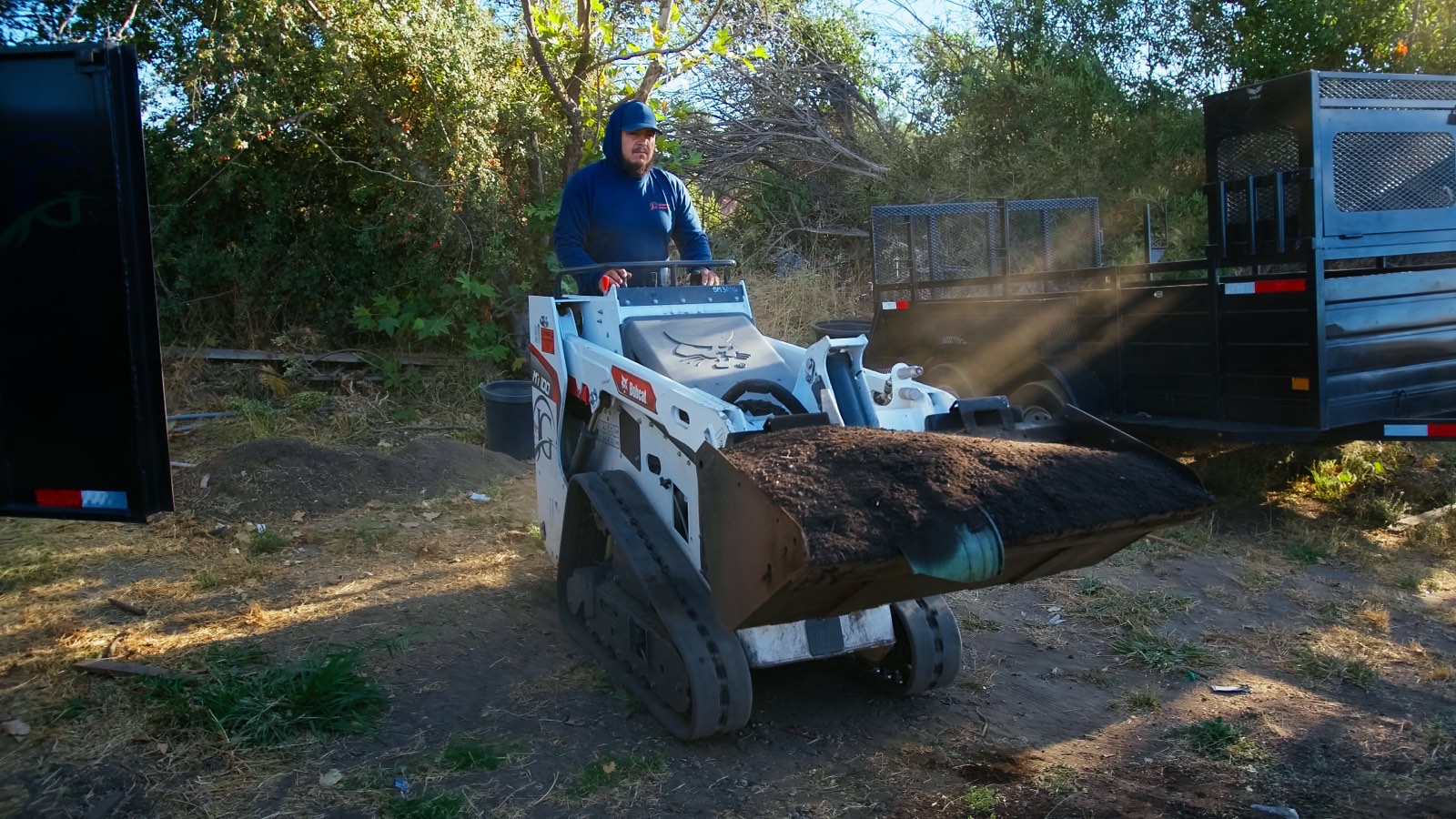 JG Landscape Management crew operating a mini track loader hauling material on a job site